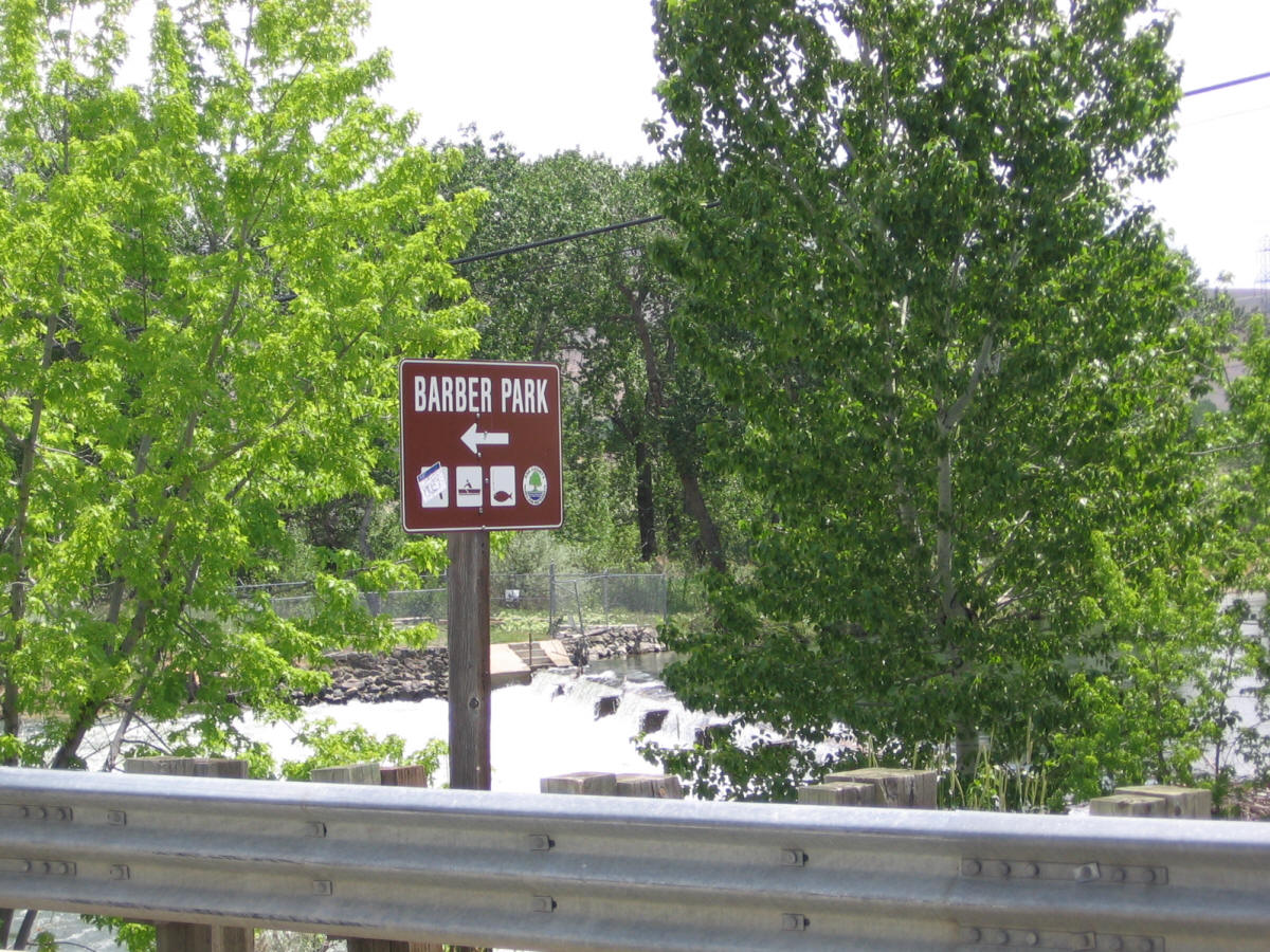 Barber Park directional sign amid trees near a rocky river flow